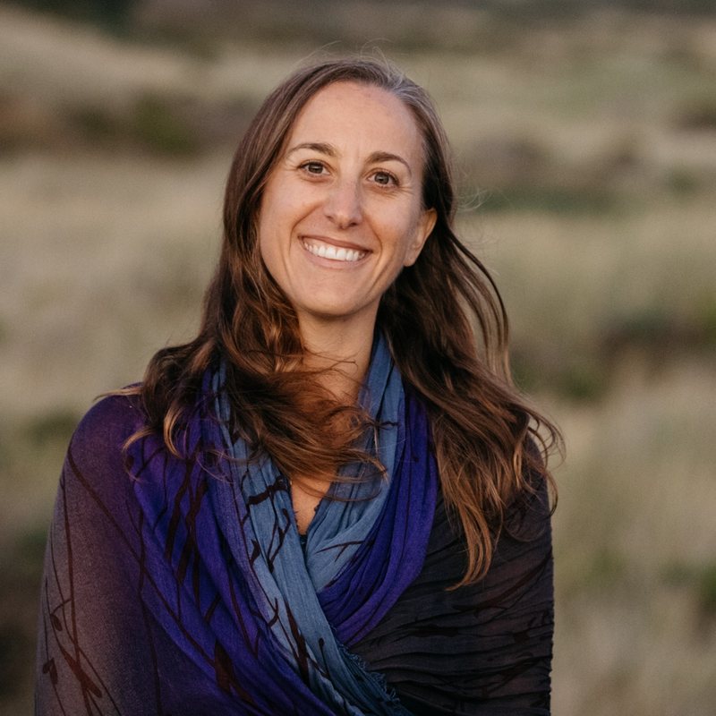 Estee Fletter, vinyasa yoga teacher at The Castro Room in San Francisco, smiling outdoors in a coastal meadow, wearing a blue scarf