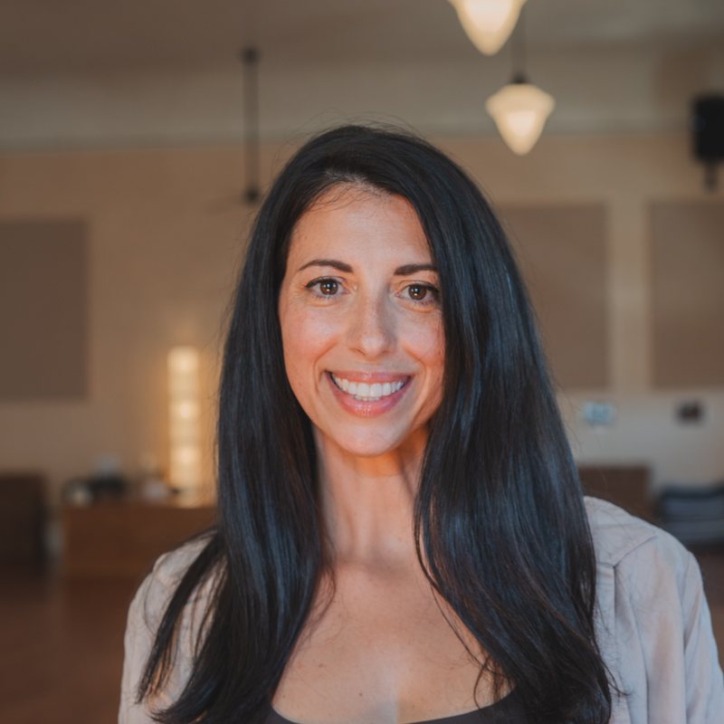 Giana Gambino, vinyasa yoga teacher at The Castro Room in San Francisco, smiling, with long dark hair, in the practice room at The Castro Room
