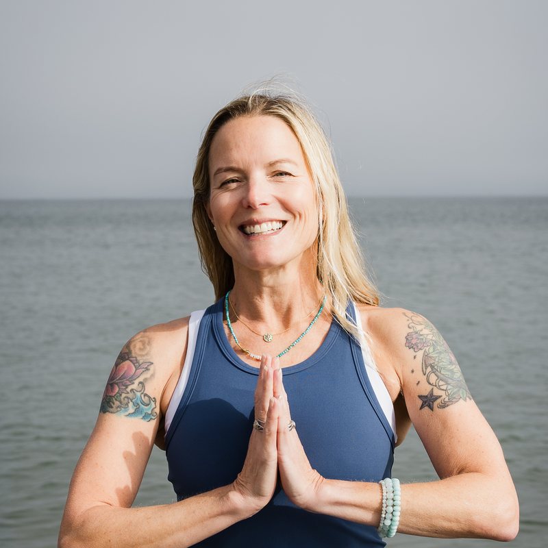 Hope Van Sciver, vinyasa yoga teacher at The Castro Room in San Francisco, smiling with hands pressed together at the heart in front of the ocean