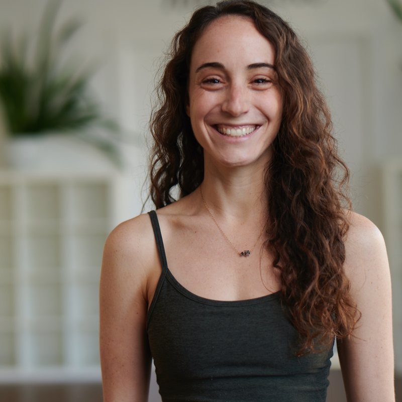 Lauren Cohen, vinyasa yoga teacher at The Castro Room in San Francisco, smiling broadly, with long curly hair, in a dark tank top
