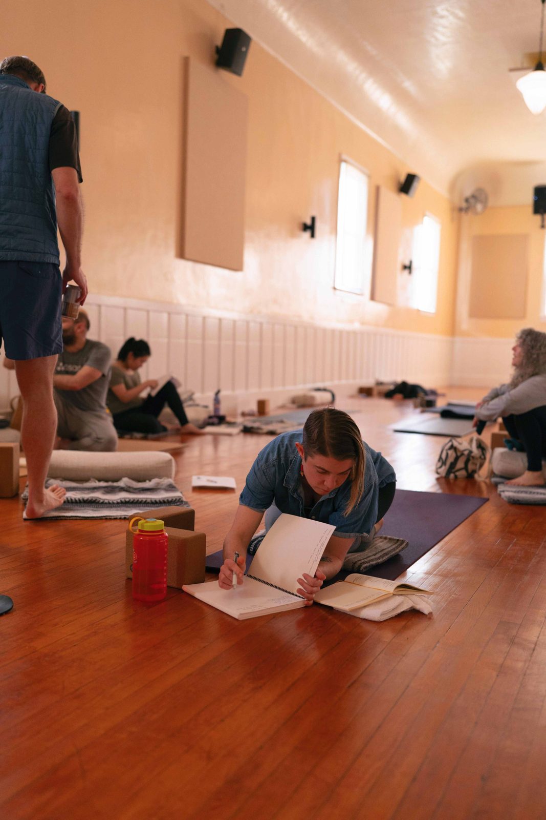 A yoga teacher training student writes in an open notebook on the studio floor