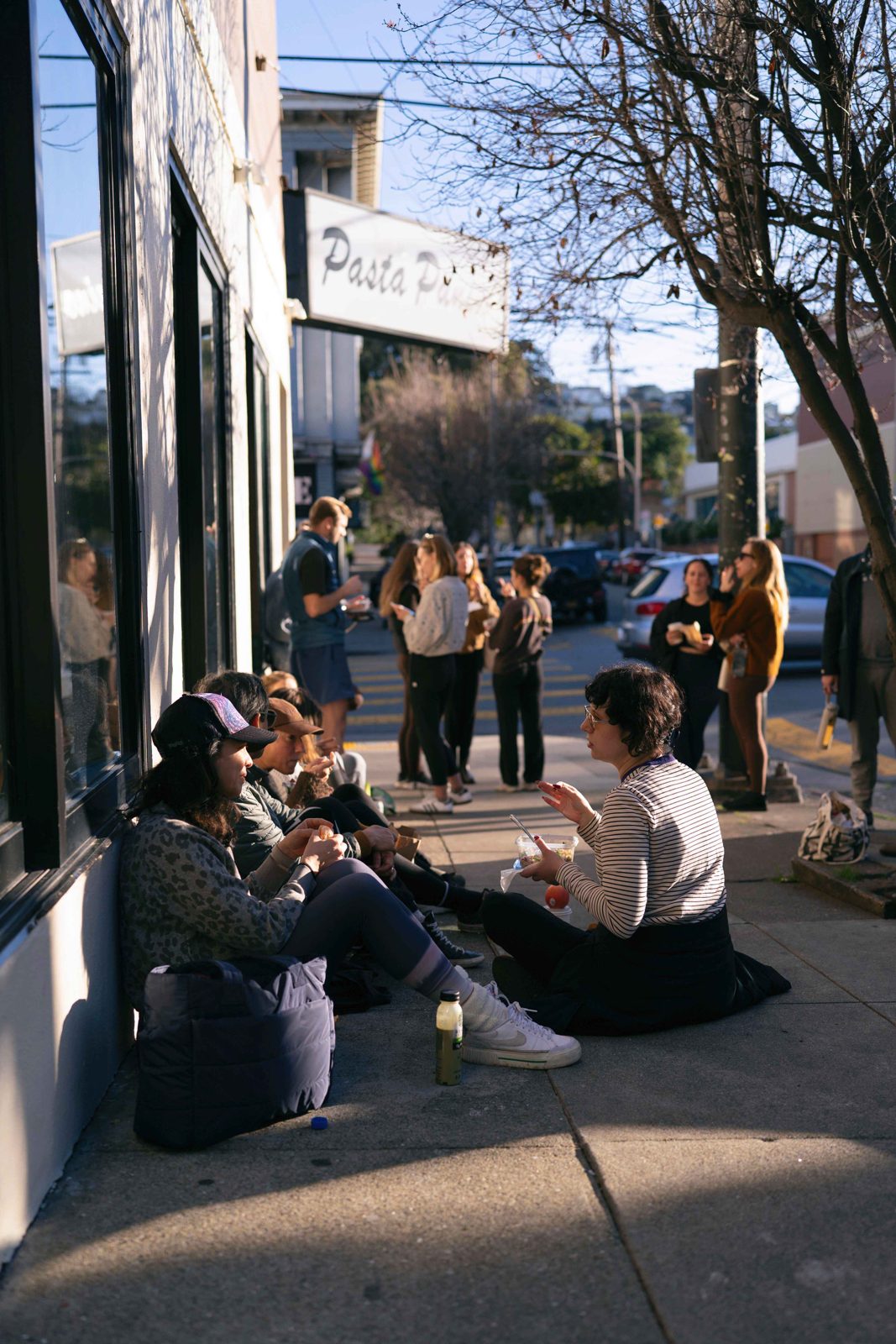 Yoga teacher training students eating lunch on the sunny sidewalk outside The Castro Room