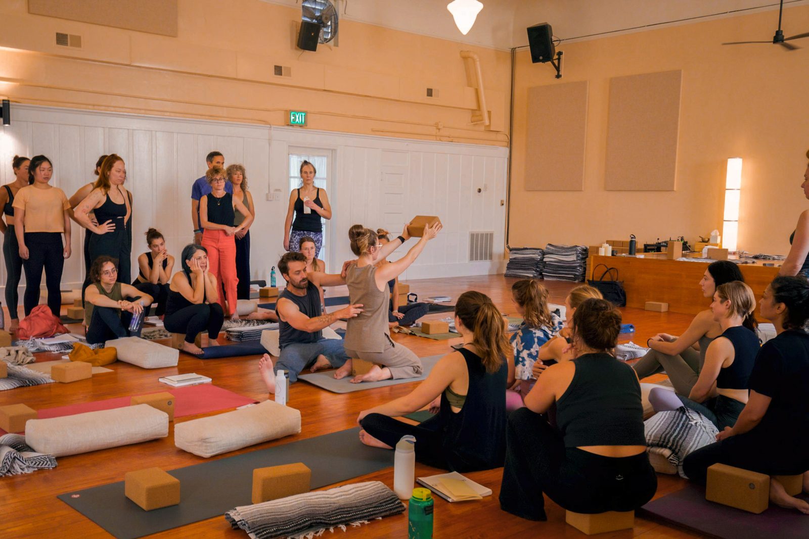 Students gather around the studio floor to watch a teaching demonstration during yoga teacher training